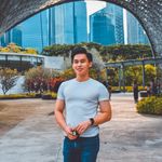 A young man stands confidently under a geometric structure with a city skyline backdrop, showcasing urban fashion and architecture.
